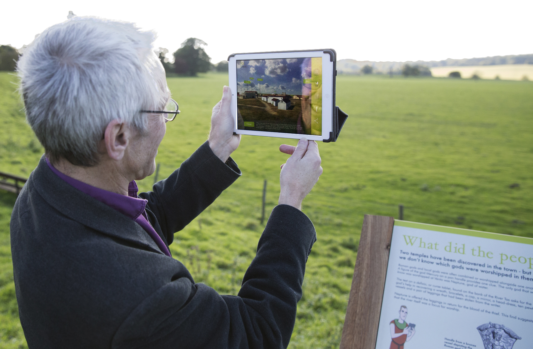 A man looks at an iPad showing a roman town overlaying existing fields
