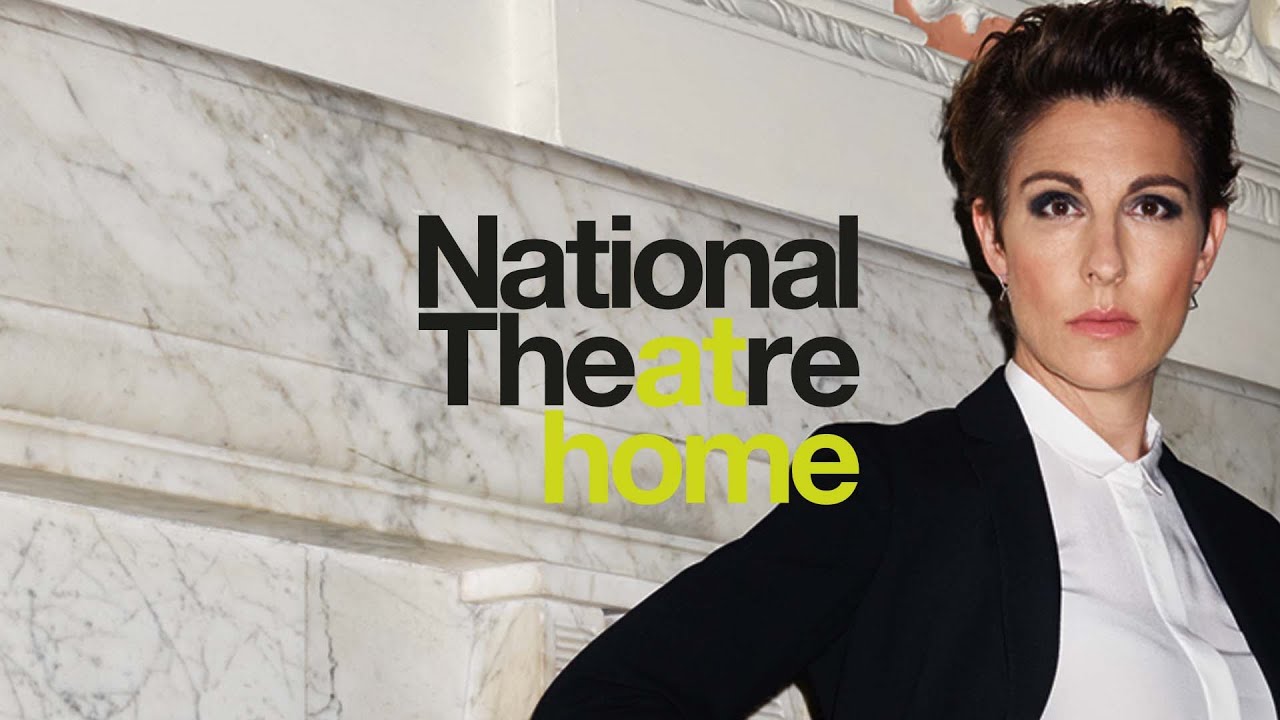 A woman standing next to the words 'National Theatre At Home'