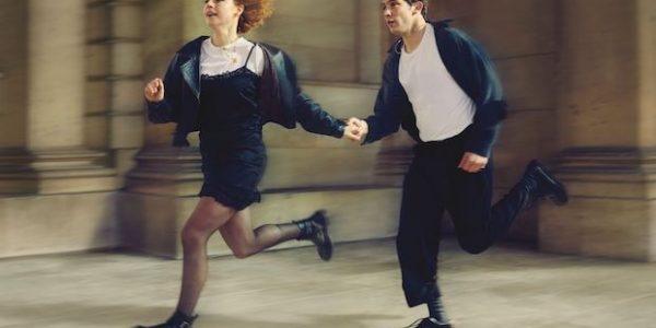 A young woman and man run down a street holding hands
