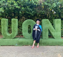 Olivia in a graduation gown standing in front of large green letters, UON