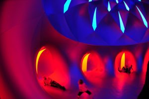 Inside a Luminarium, people lying inside blue, red and yellow chambers with slits of blue light above