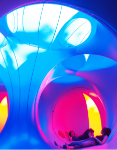 Inside a Luminarium, blue, pink and yellow columns and chambers with light pouring in above, people lying down