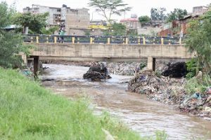 Bridge over river with brown water and piles of rubbish at side, Kenya