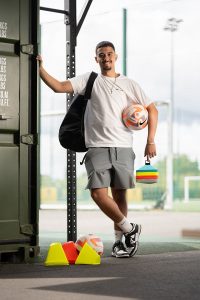 Daniel Damesceno de Faria leaning on a wall holding a ball in he other hand with red and yellow cones on the ground