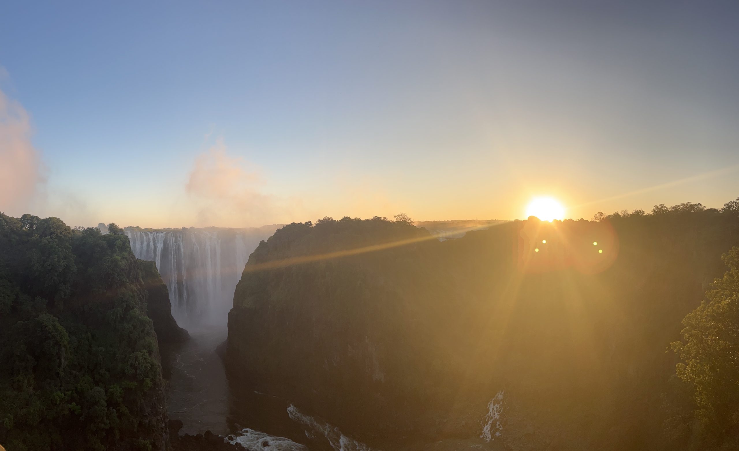 Victoria Falls at sunrise, large waterfall with trees on either side
