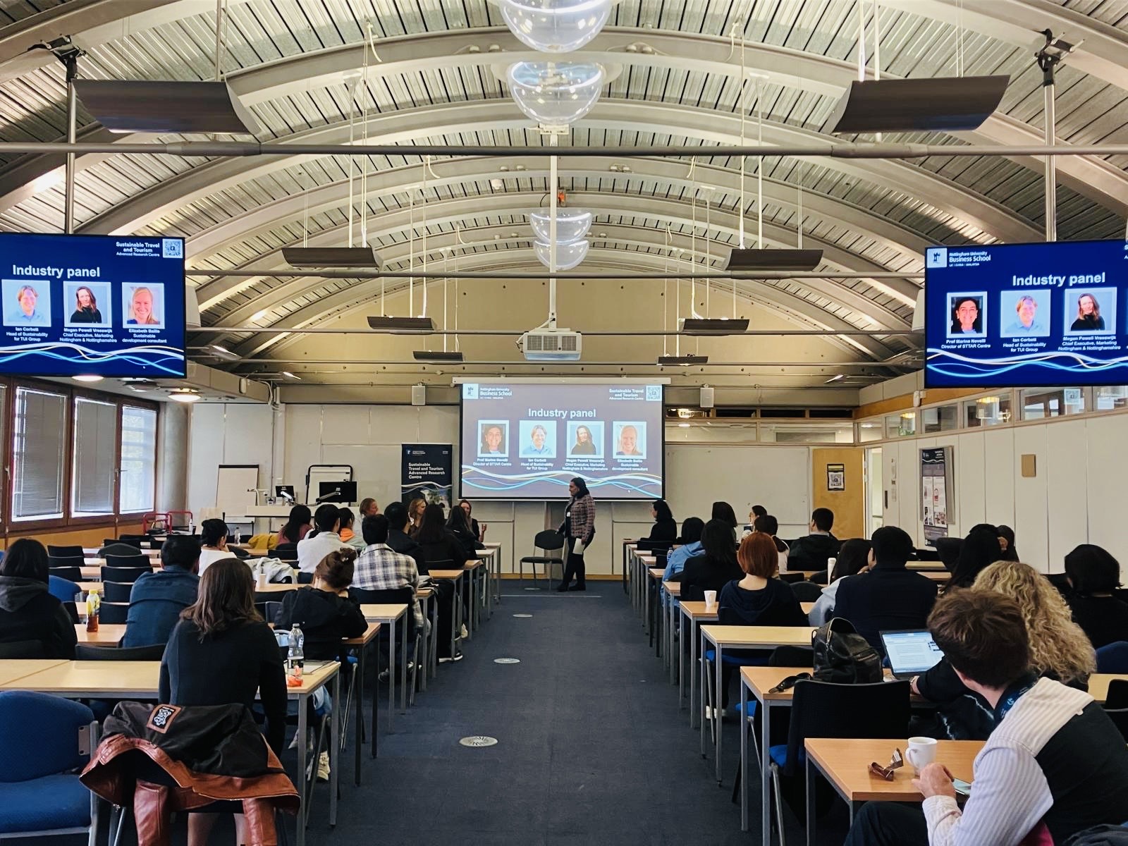 Marina Novelli at the front of a large lecture theatre for World Tourism Day 2025 with rows of students sat at tables facing the front with large screens at the front and sides