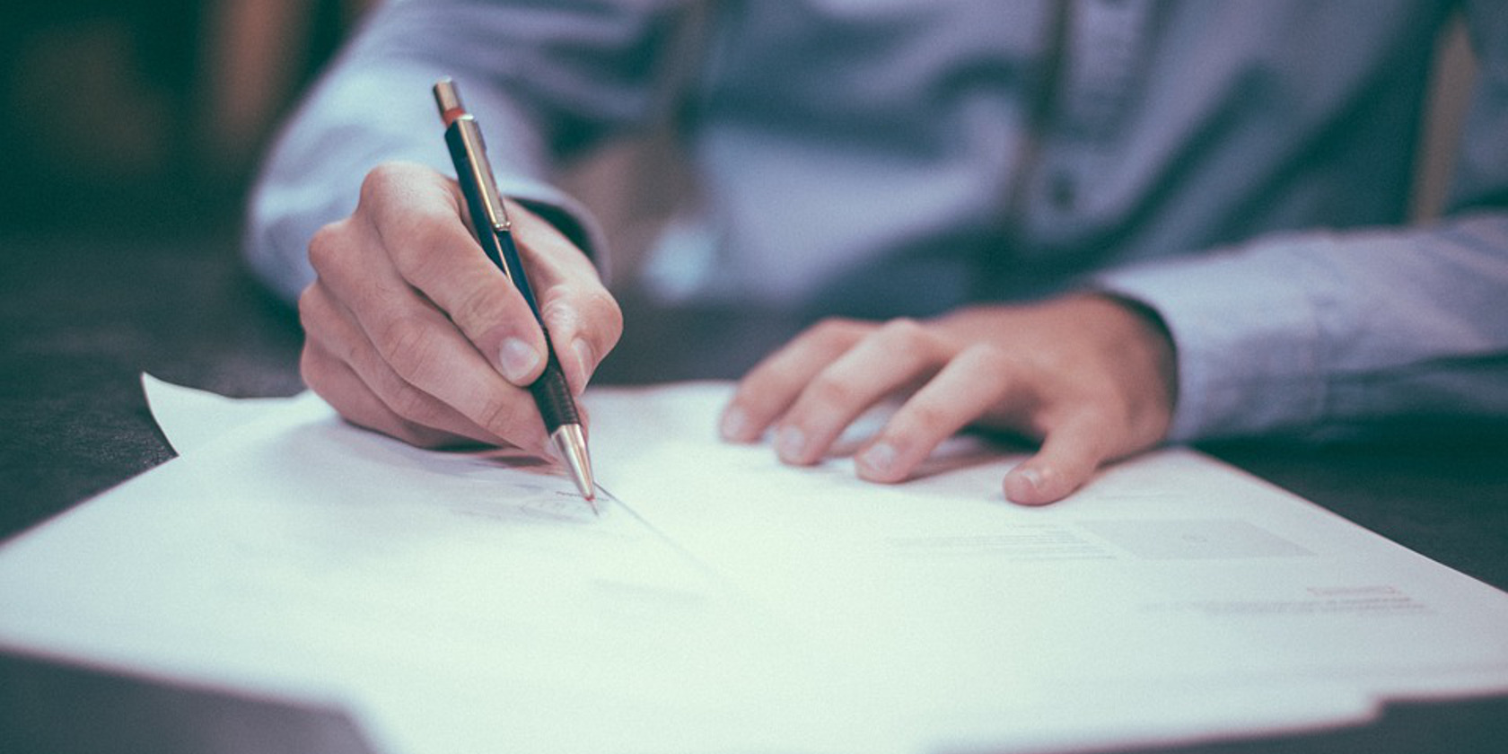 A man dressed smartly writing out his CV with a pen and paper