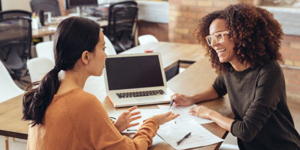 Two women looking at each other laugh over some work
