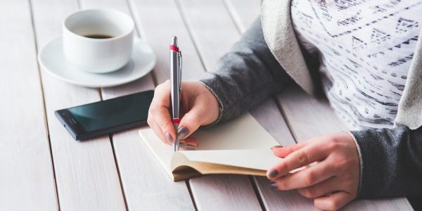 Person writing notes on a table with a coffee