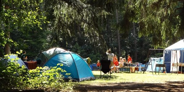 People sitting on the grass around tents at a summer camp