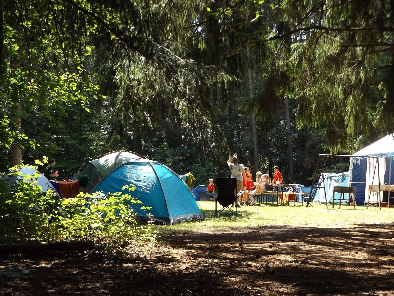 People sitting on the grass around tents at a summer camp