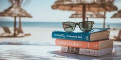 sunglasses placed on top of a stack of colourful books with sunny beach background