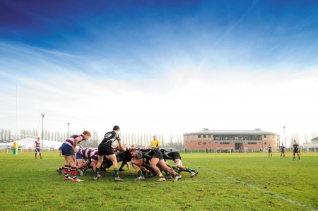 Rugby men in a huddle on a rugby pitch with blue skies