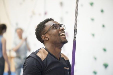 A man with a rope tied to him looking up at a climbing wall.