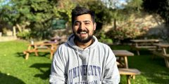 An image of Aditya sitting outside on a bench in his University of Nottingham grey hoodie