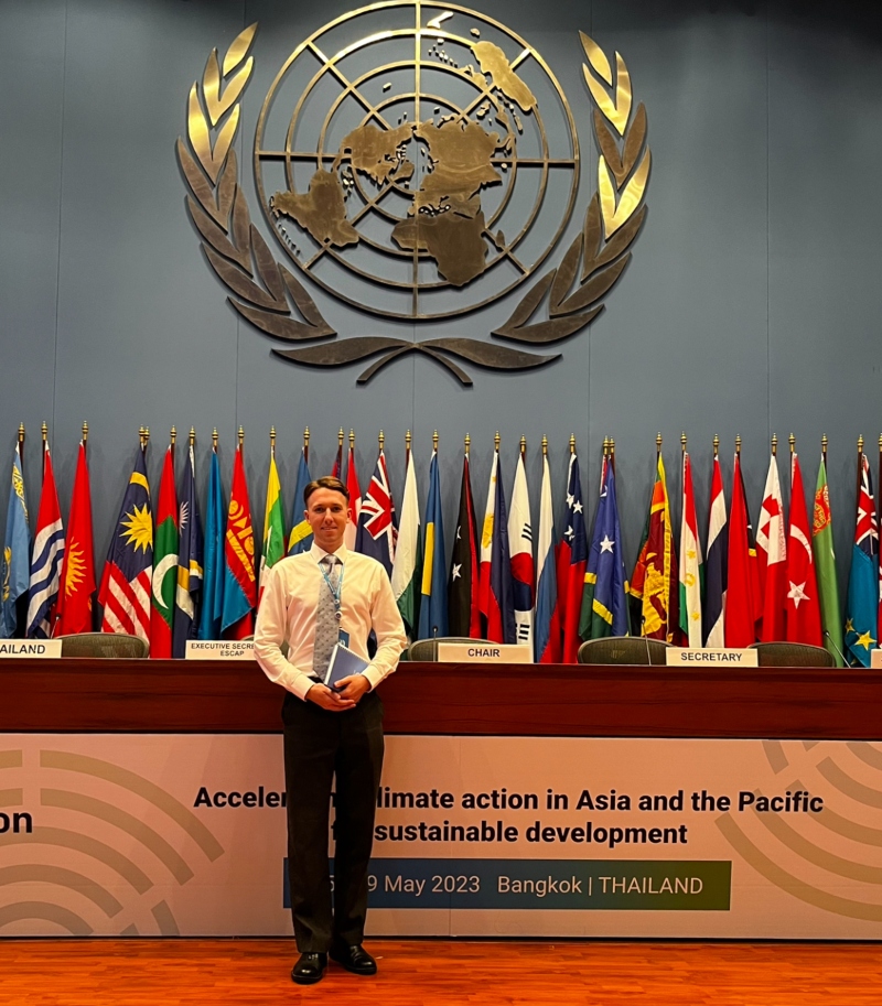 Jack Crawford at the UNI standing in front of the UN logo and national flags