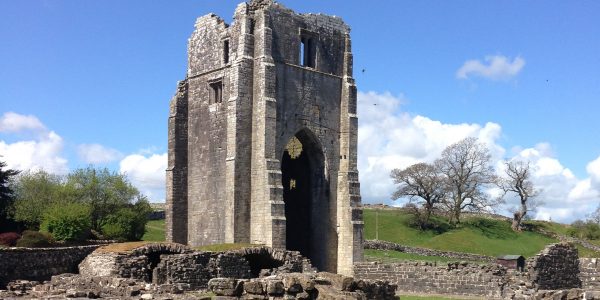 A large central, but ruined tower, with low level walls in the foreground, and a beautiful blue sky beyond.