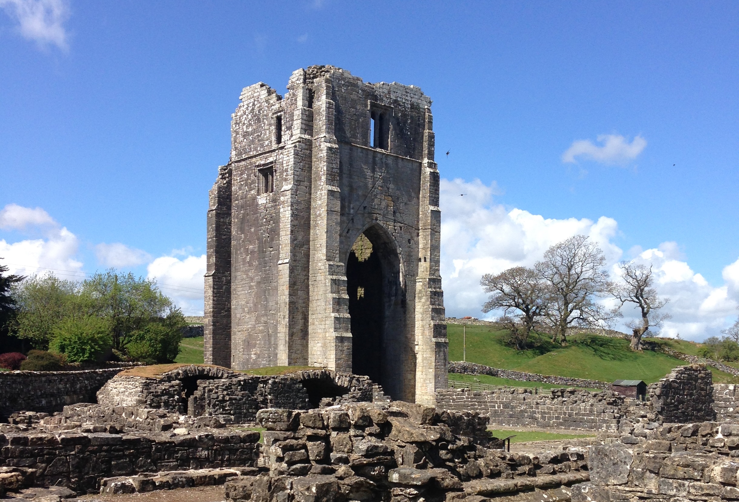 A large central, but ruined tower, with low level walls in the foreground, and a beautiful blue sky beyond.
