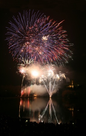 several fireworks explode, reflected in a lake
