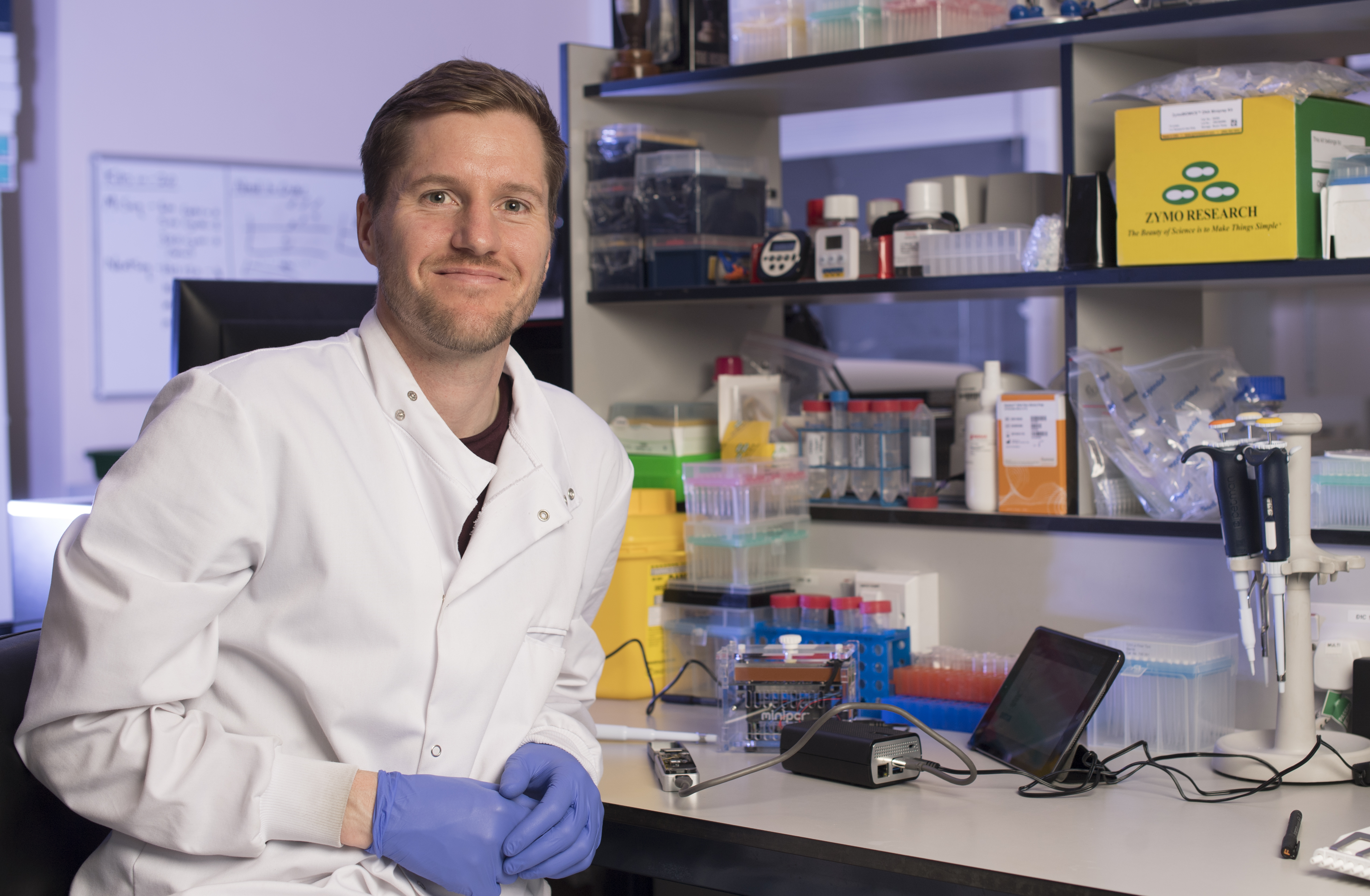 Dr Chris Moore sitting at his work bench with the Oxford Nanopore MinION