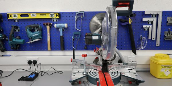 A saw on a workbench with blue board behind holding tools