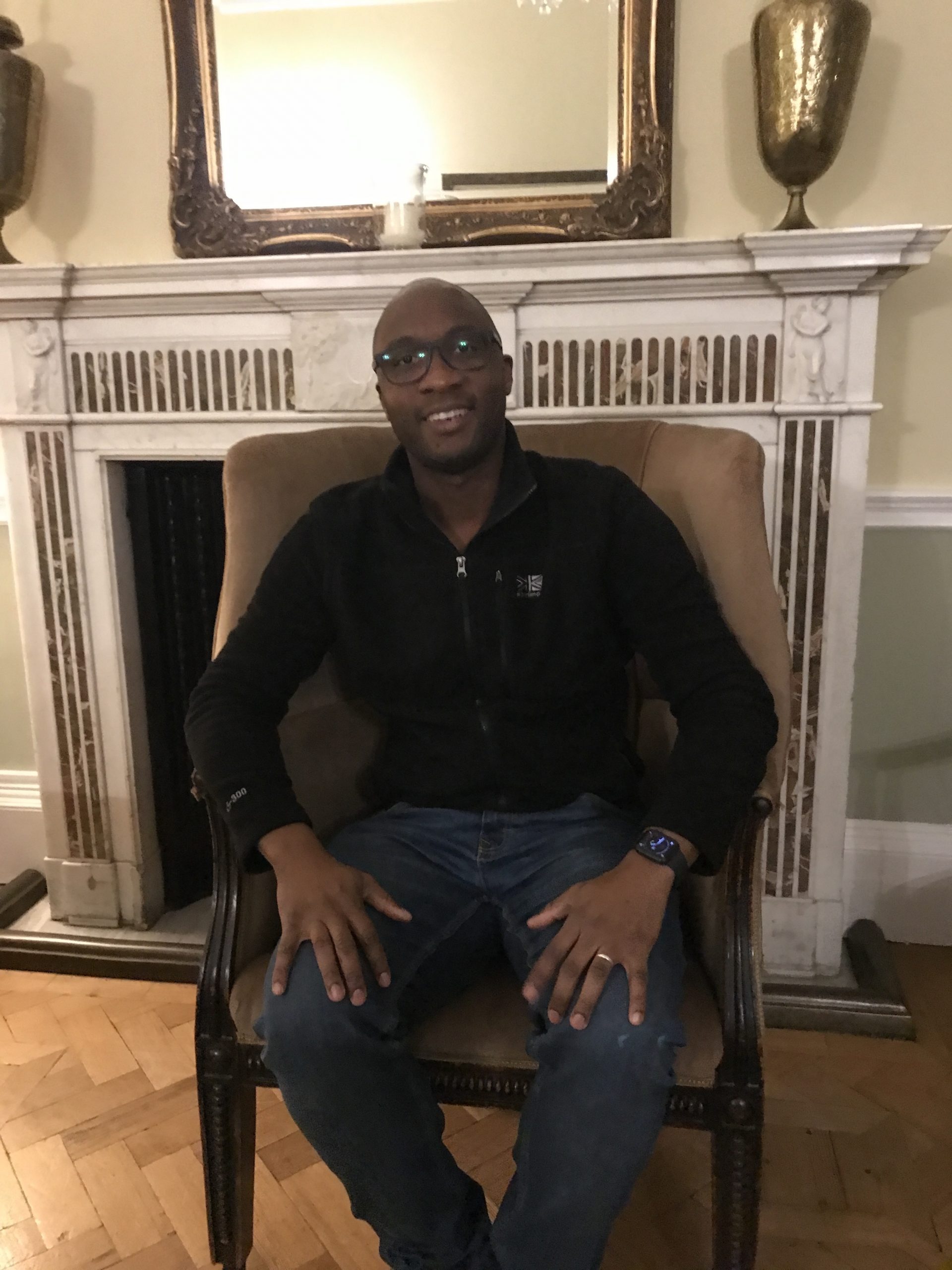 Chris Chagumaira a dark-skinned man, sits in a chair wearing a black jumper