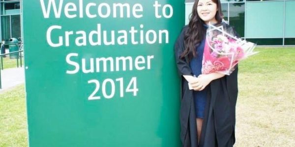 Physiotherapy graduate holding a bouquet of flowers next to a 'Welcome to Graduation Summer 2014' sign