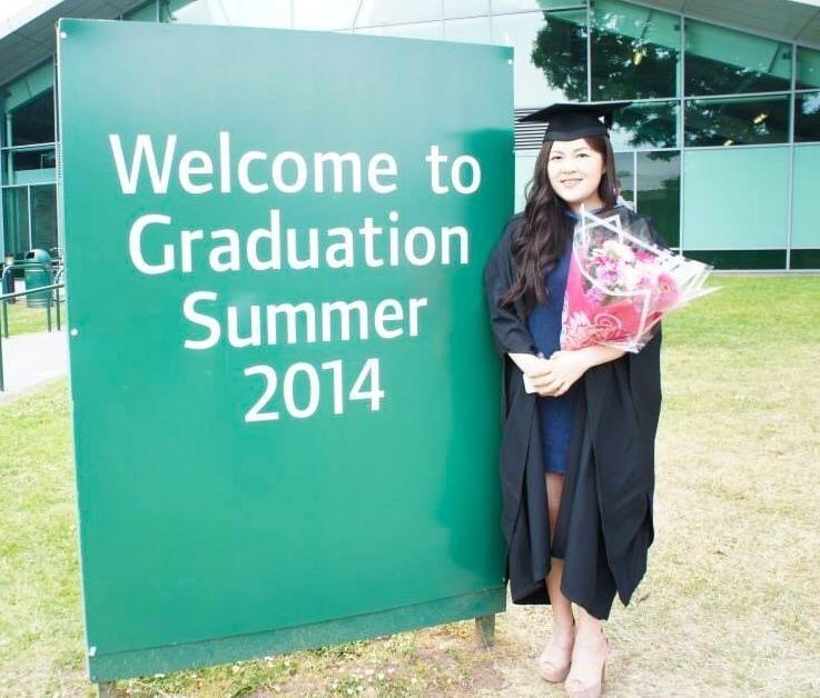Physiotherapy graduate holding a bouquet of flowers next to a 'Welcome to Graduation Summer 2014' sign