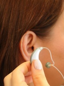 Side of someone's head showing the ear and someone holding a hearing aid near to it