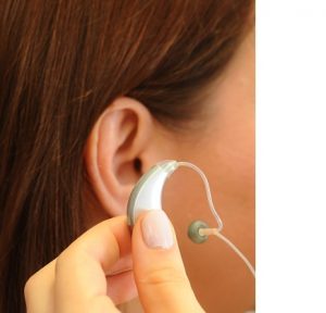 Side of someone's head showing the ear and someone holding a hearing aid near to it