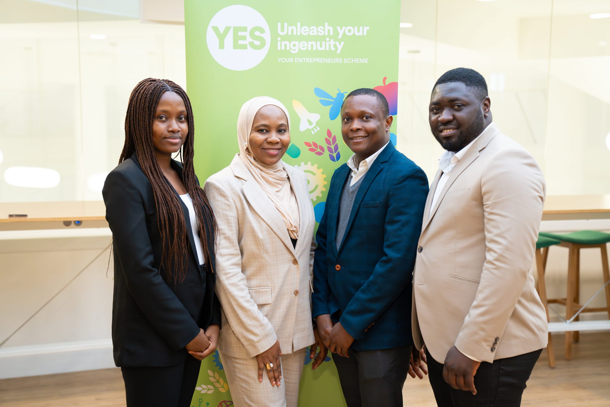 The four team members pose for a photo in front of the YES banner