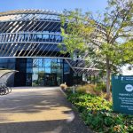 A landscape shot of The Ingenuity Centre in the sunshine, with the trees blooming in green in front