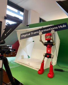 A toy lego-like robot, holding up a sign saying 'digital transformations hub'.