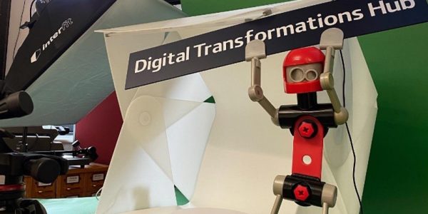 A toy lego-like robot, holding up a sign saying 'digital transformations hub'.