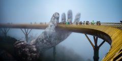 curved bridge with people walking over it while a huge hand holds it up
