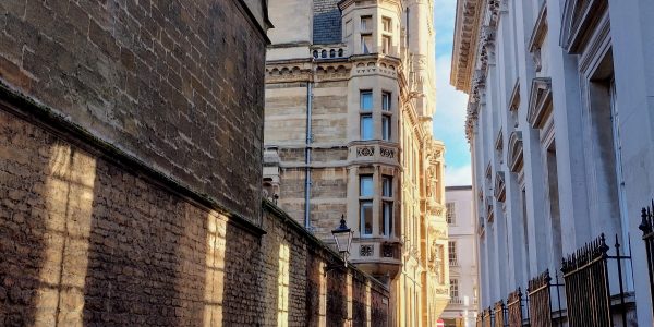 Rainy street in Cambridge (Senate House Passage) with cyclist in the distance and sun making window patterns on wall