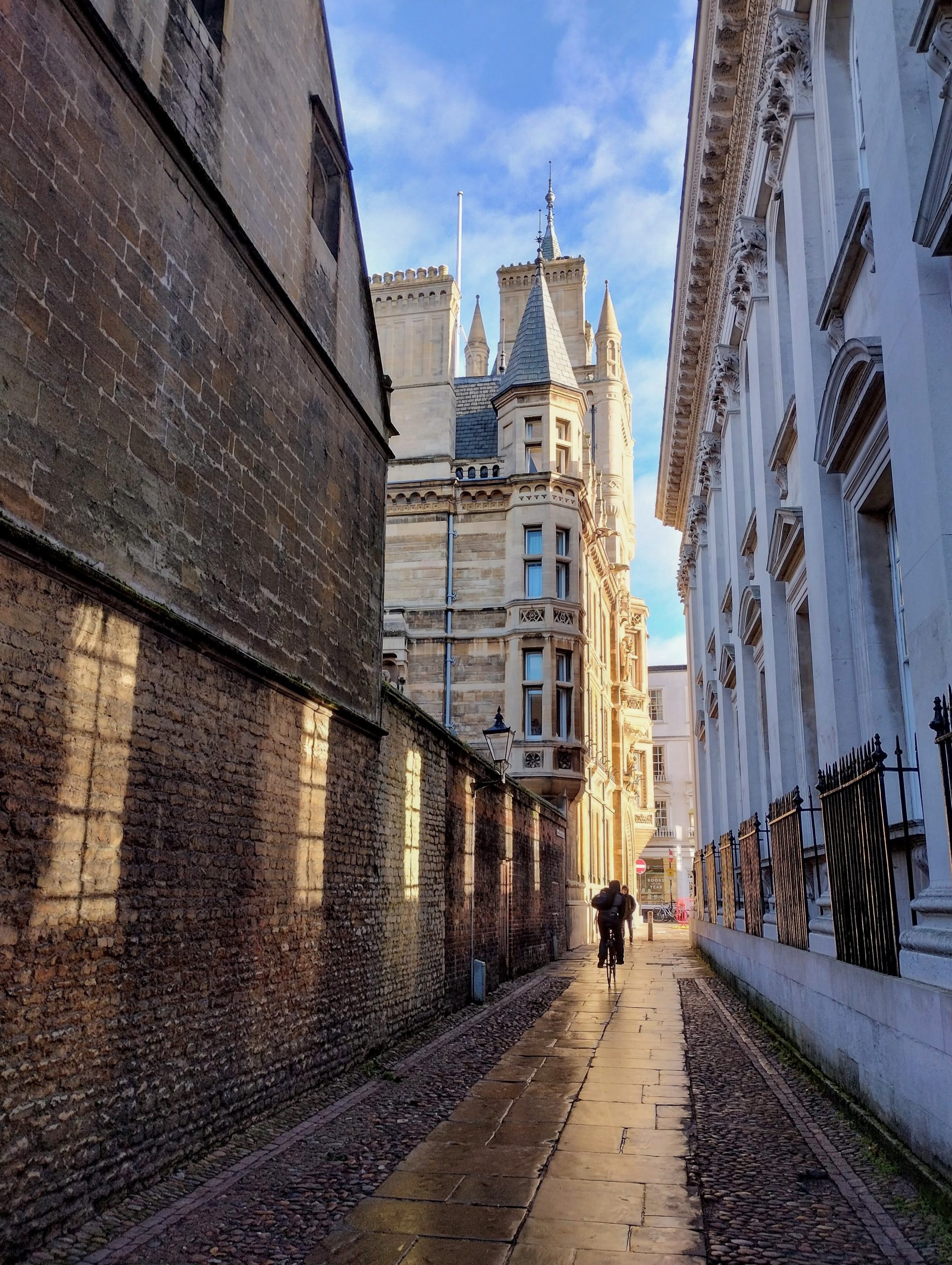 Rainy street in Cambridge (Senate House Passage) with cyclist in the distance and sun making window patterns on wall