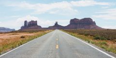 straight American road leading to Monument Valley mountains on the horizon