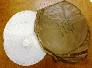 Two circular paper weir gauge charts, extracted from a larger bundle wrapped in brown paper