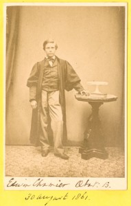 Photograph of Edwin Chamier as a young boy, wearing a long robe, standing with one hand resting on a side table. The photograph is stuck into an album. (Ref: Ca D 23)