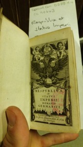 Photo of a hand holding open the frontispiece of a volume, with cherubs surrounding text in Latin