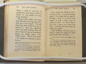 Open pages of the book held by weights, text discussing angels taking the souls of sick children
