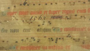 Medieval music staves with the Latin words written in red ink, with the date and title of the later book it was bound into written across in black ink