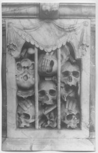 Carved skulls and boney hands peeking out beneath a carved curtain