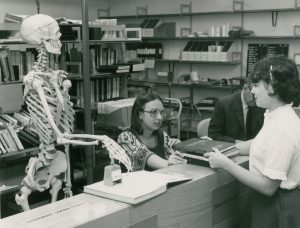 Female librarian and a skeleton issuing a book to a female student