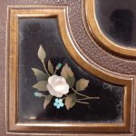 Close up of a black enamel panel with white and blue flowers set into the cover of a photo album