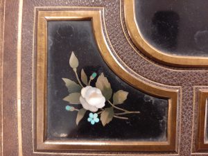 Close up of a black enamel panel with white and blue flowers set into the cover of a photo album