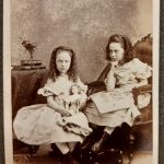 Carte de visitie showing two girls seated holding a doll and a book, labelled Louise and Mary