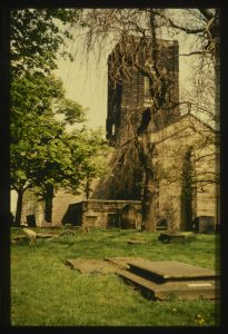 Colour photo of the church tower in summer, with graves in the foreground.