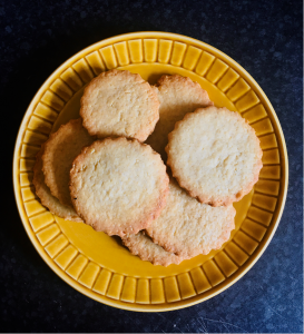 Photo of a plate of round biscuits with fluted edges, on a yellow plate on a dark kitchen counter